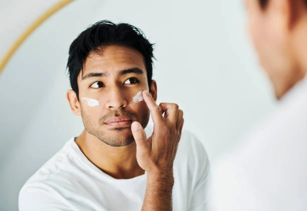 Homme appliquant délicatement une crème hydratante sur son visage devant un miroir