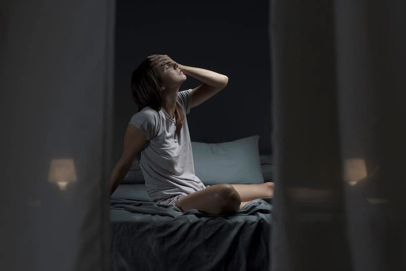 Femme assise sur son lit en pleine nuit, cherchant à dormir malgré la chaleur et les températures élevées de l'été
