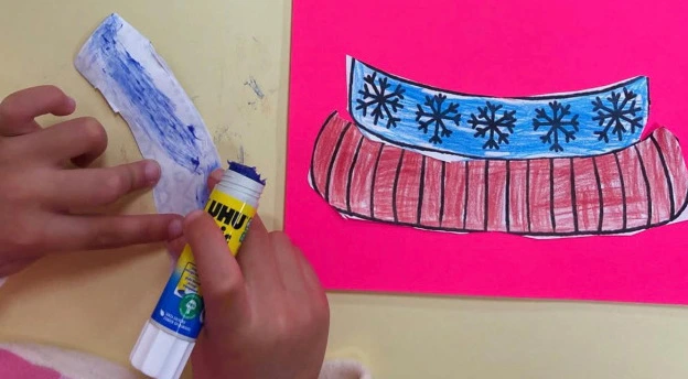 Enfant collant un bricolage colorié avec un bâton de colle UHU ReNature pendant un atelier créatif de rentrée des classes à l’école
